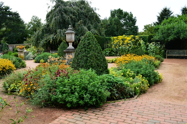 Manicured garden with vibrant flowers, trimmed shrubs, brick path, and classic stone urn centerpiece.